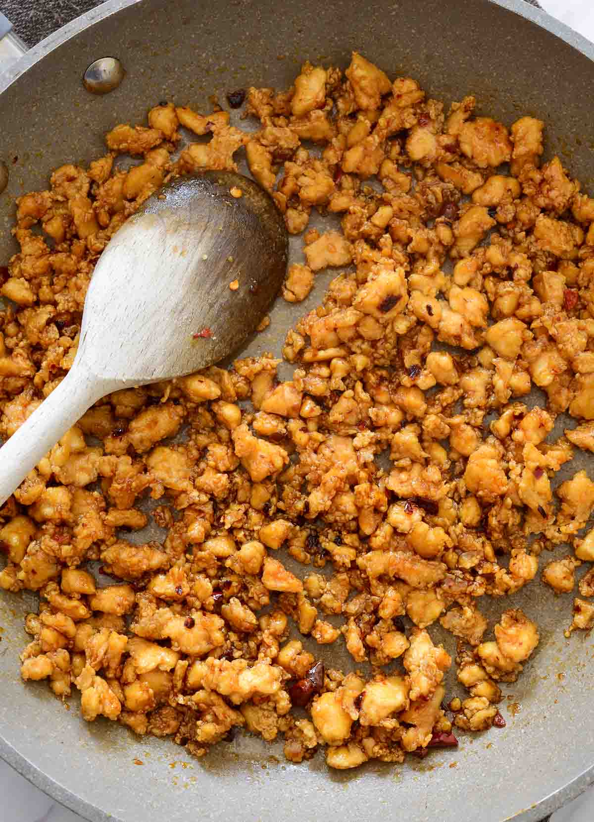 A grey pan filled with cooked tofu crumble. A wooden spoon rests inside.