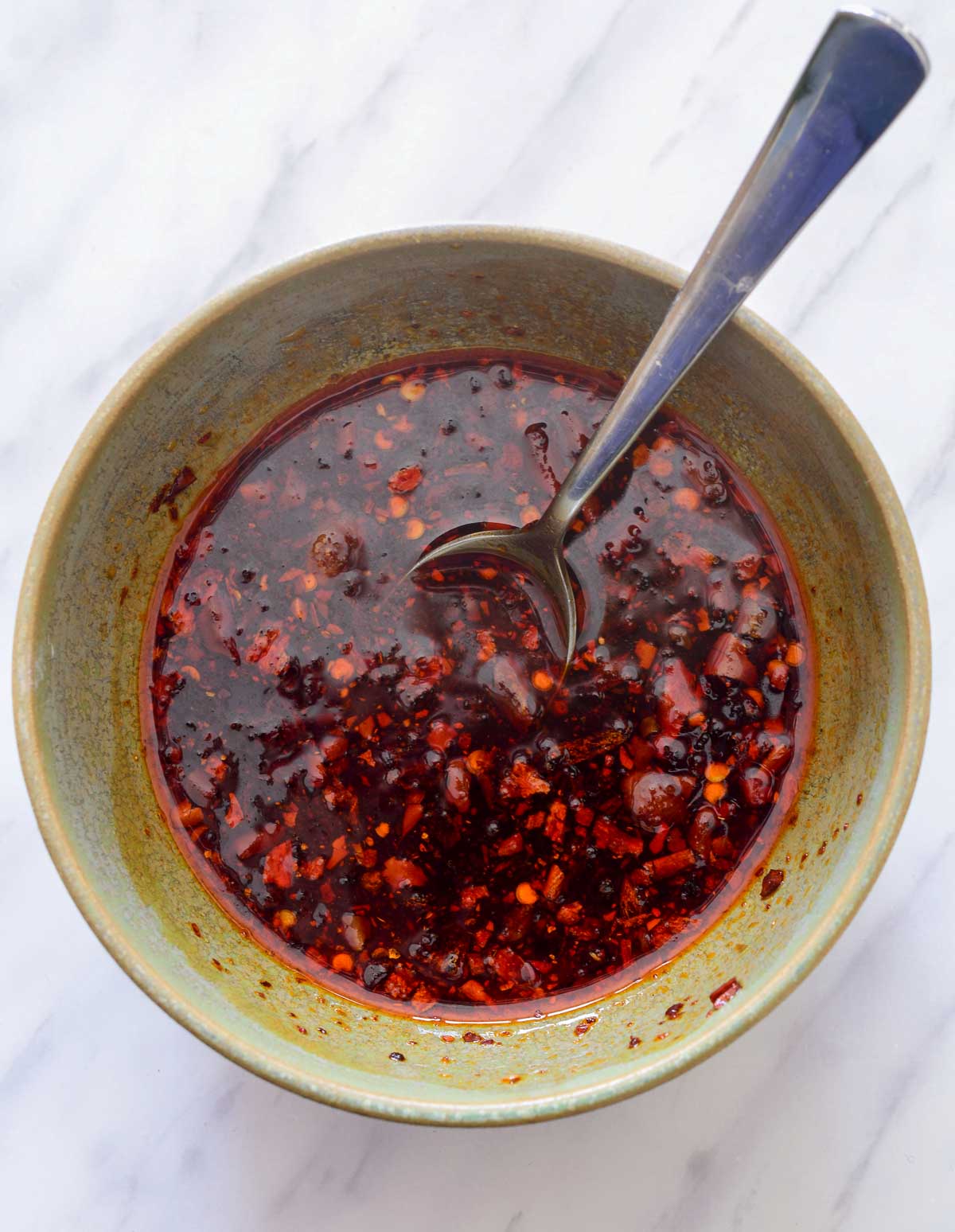 A green bowl of sauce for tofu crumble with a silver spoon in it.