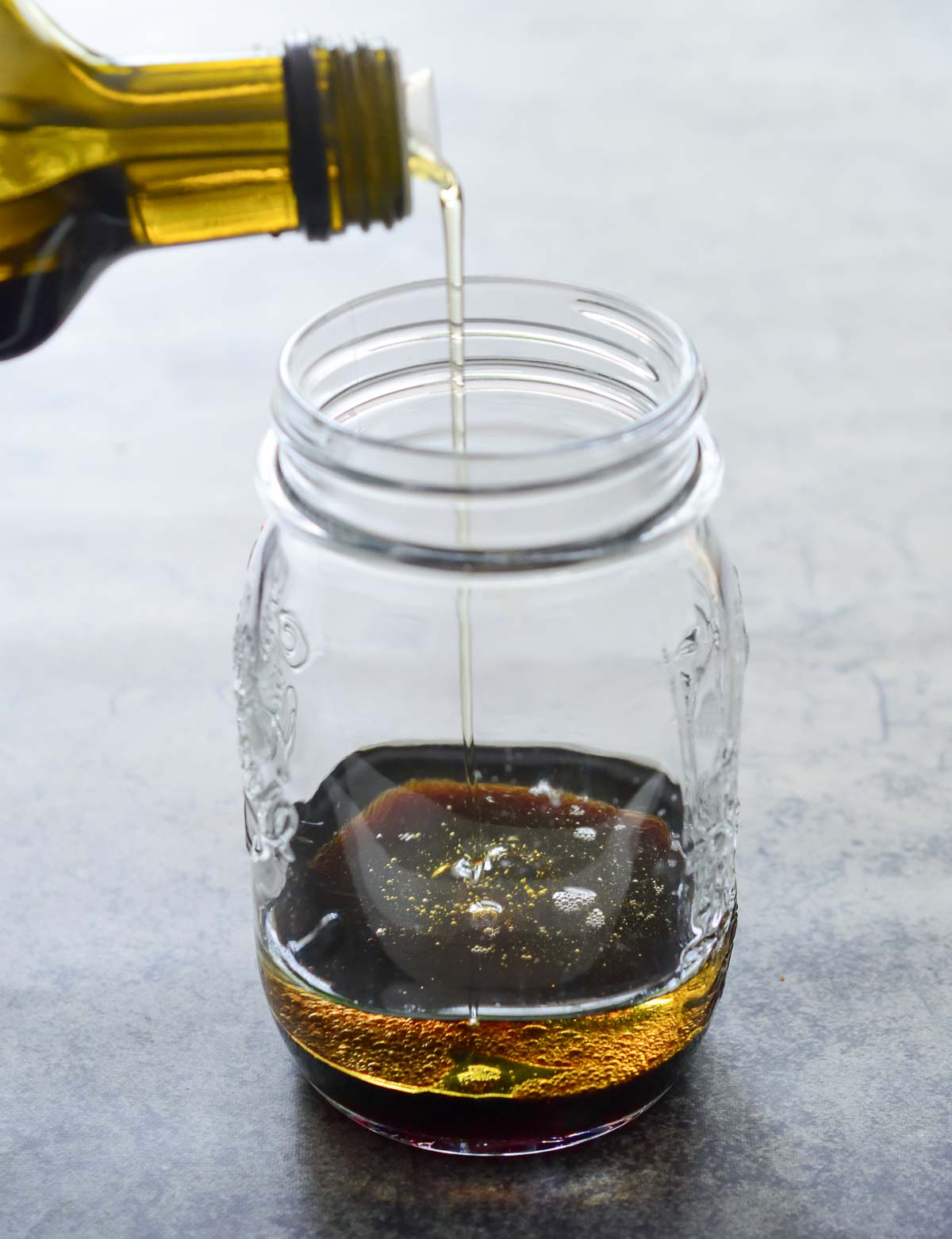 Pouring sesame oil into a clear mason jar with soy sauce in it.
