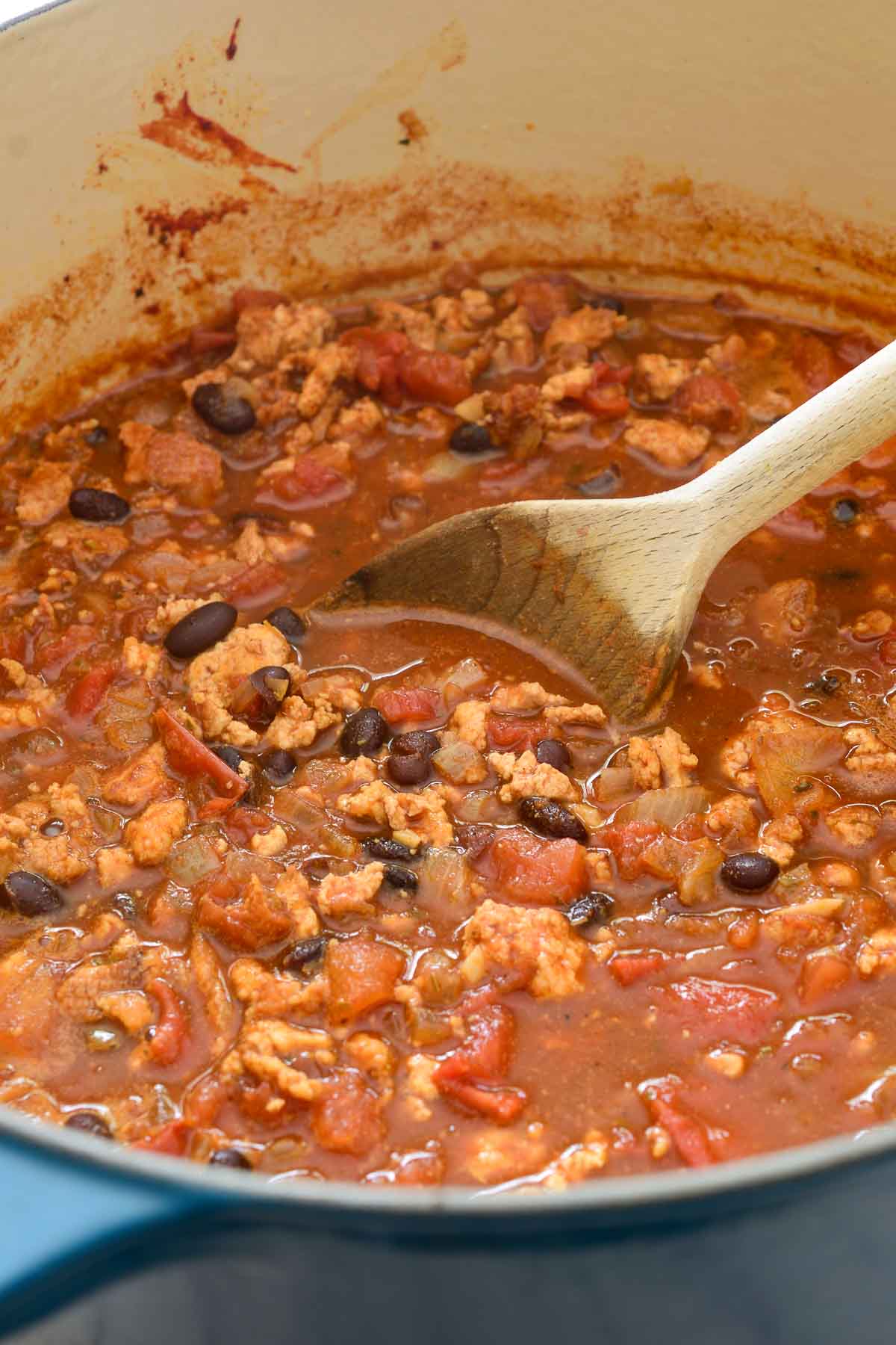 A blue pot full of tofu chili with a wooden spoon stirring it.