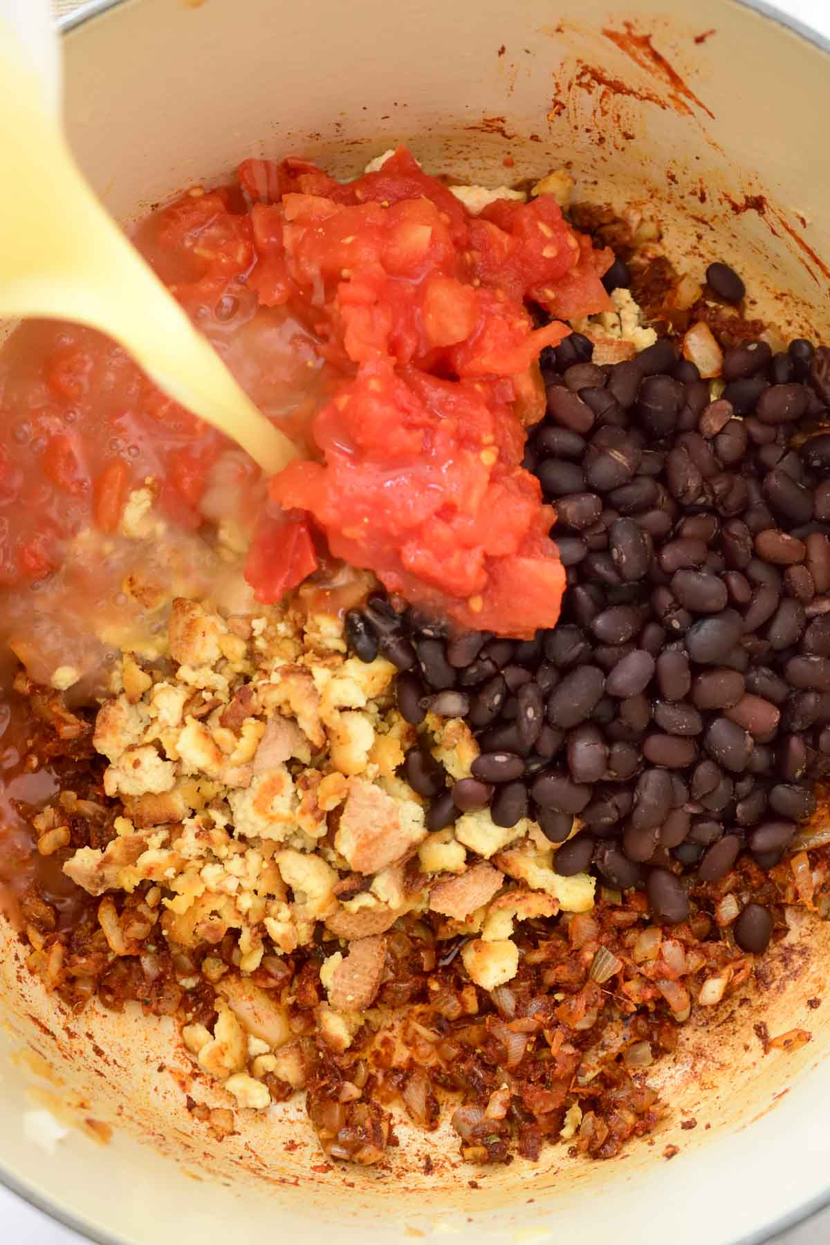 Pouring vegetable stock into the pot with smoked tofu, black beans and diced tomatoes.
