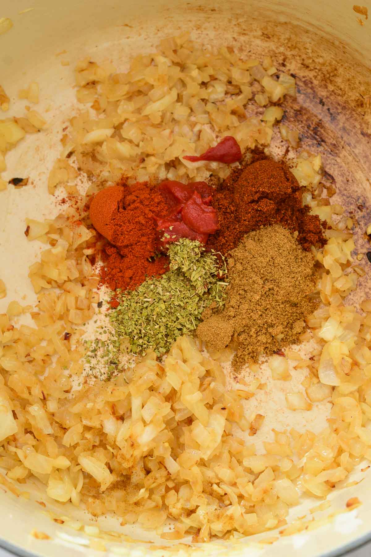 A white pot with fried onions, cumin, oregano, paprika, chili powder and tomato paste in a pile in the middle.