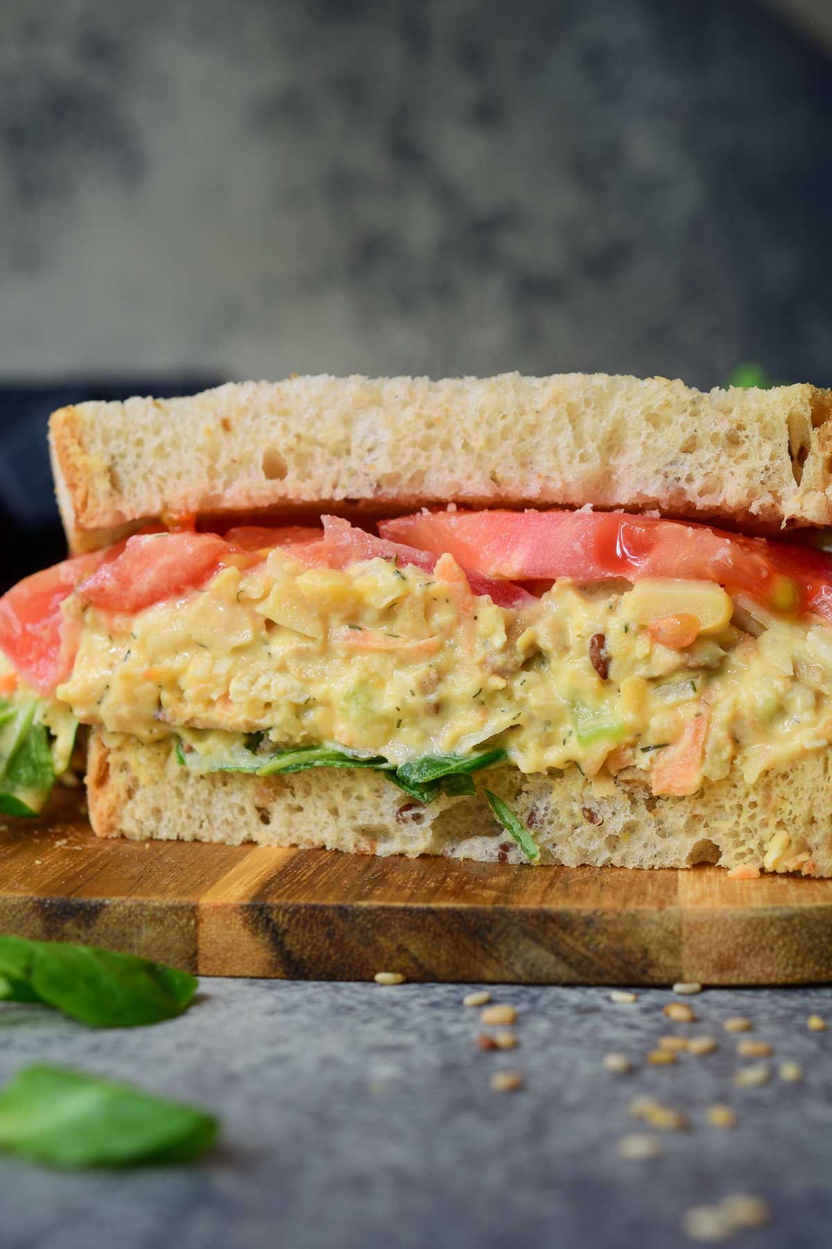 A close-up image of a smashed chickpea salad sandwich cut in half sitting on a wooden board.