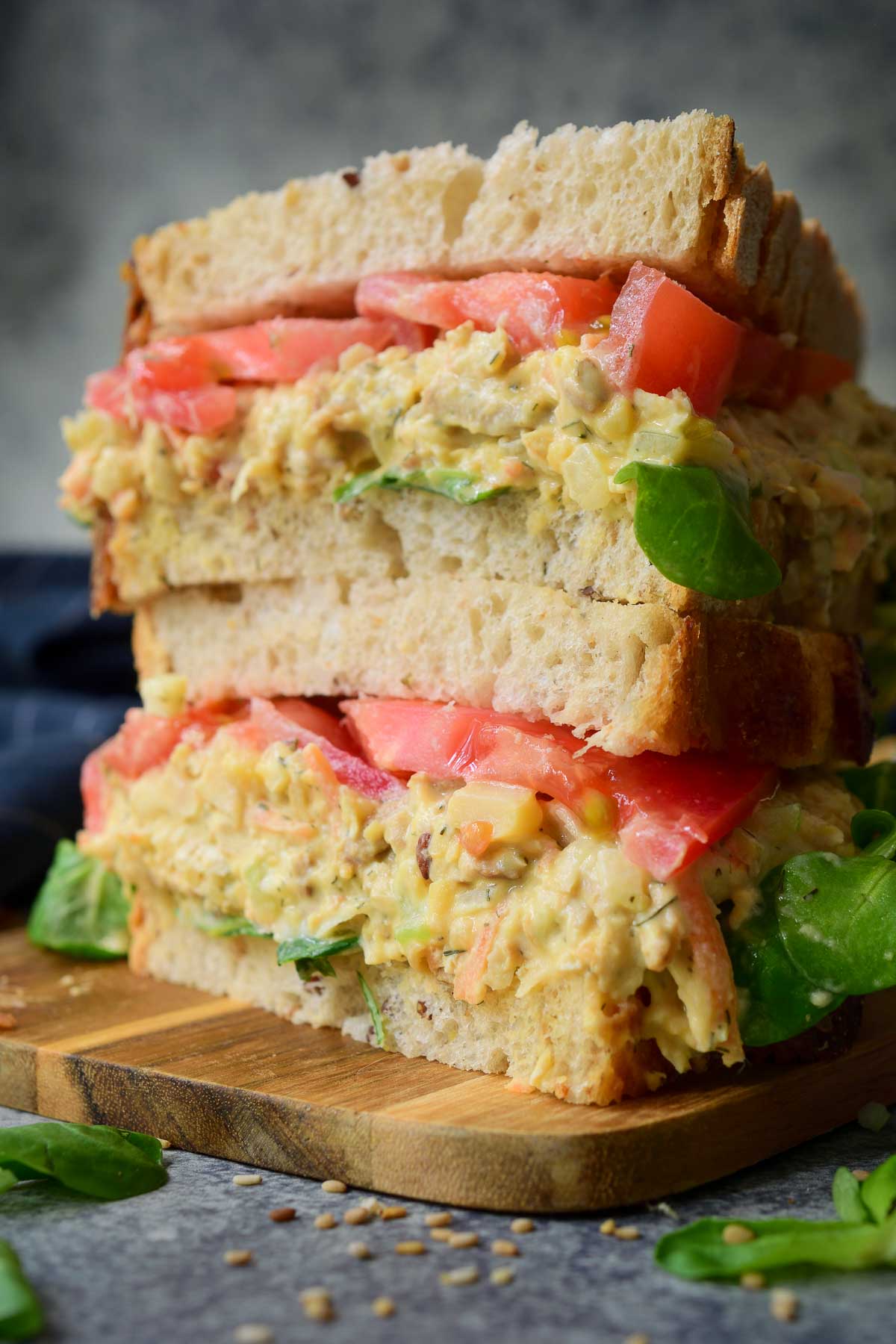 Two halves of a smashed chickpea salad sandwich stacked on top of each other on a wooden cutting board.