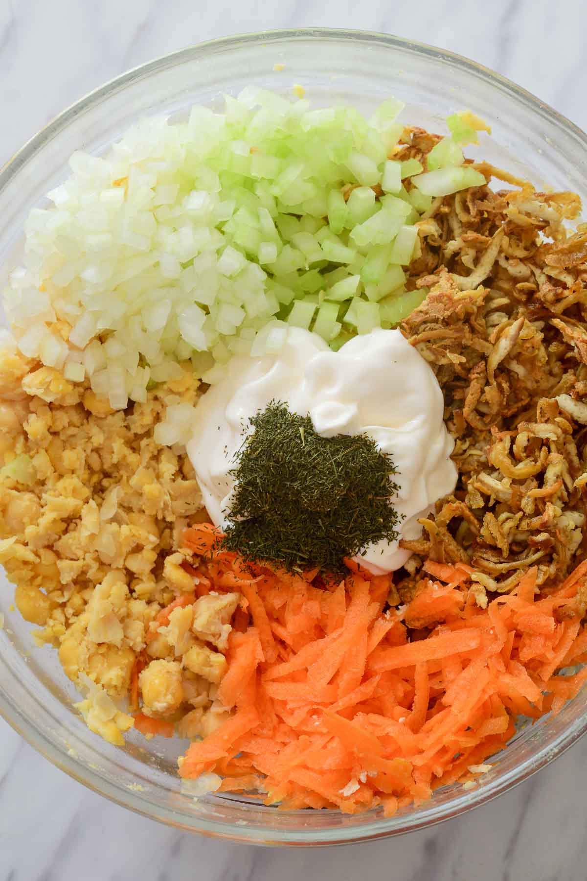All the ingredients for smashed chickpea salad separated into piles in a glass bowl.