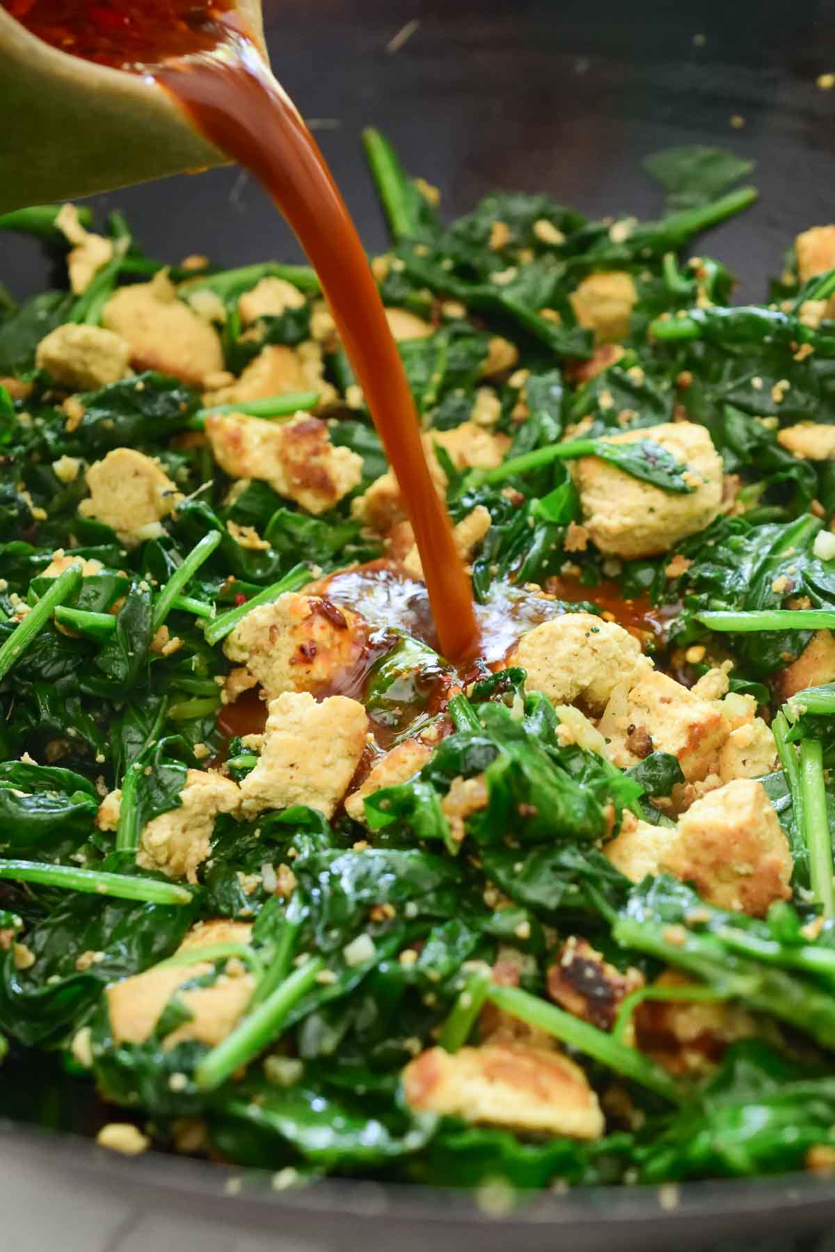 Pouring the stir fry sauce into the pan of stir fried tofu and spinach.