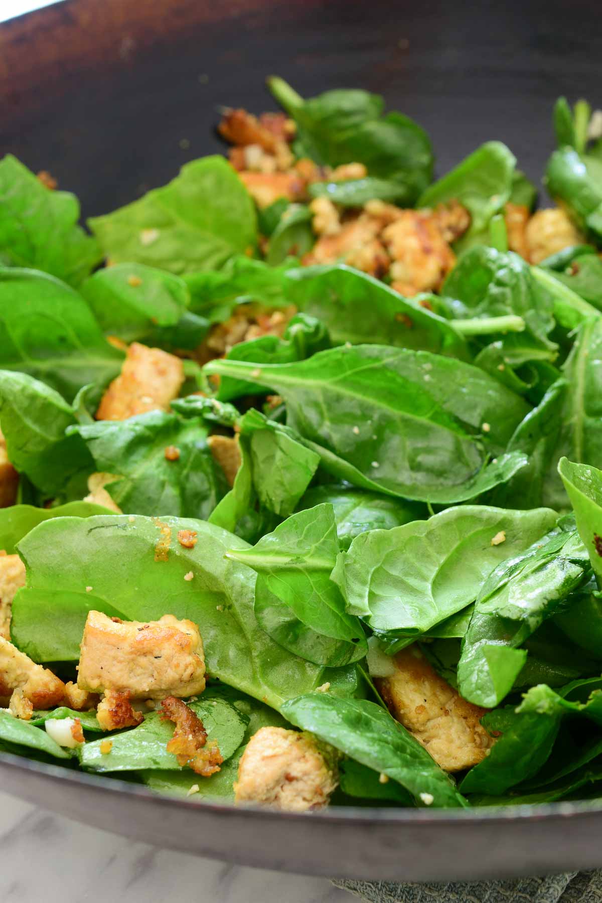 A wok filled with fried tofu and fresh green spinach leaves.