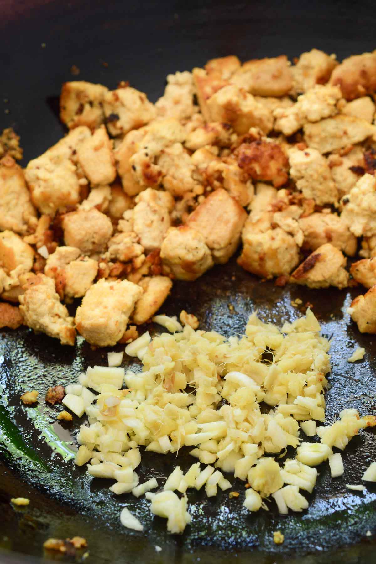 A black wok with a pile of fried tofu and a smaller pile of minced ginger and garlic.