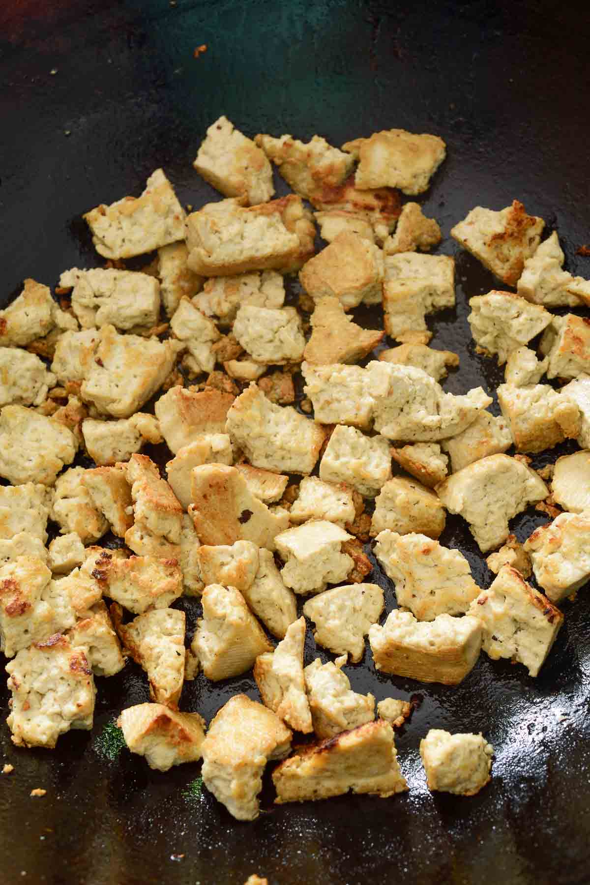 The fried tofu chunks inside a black wok.
