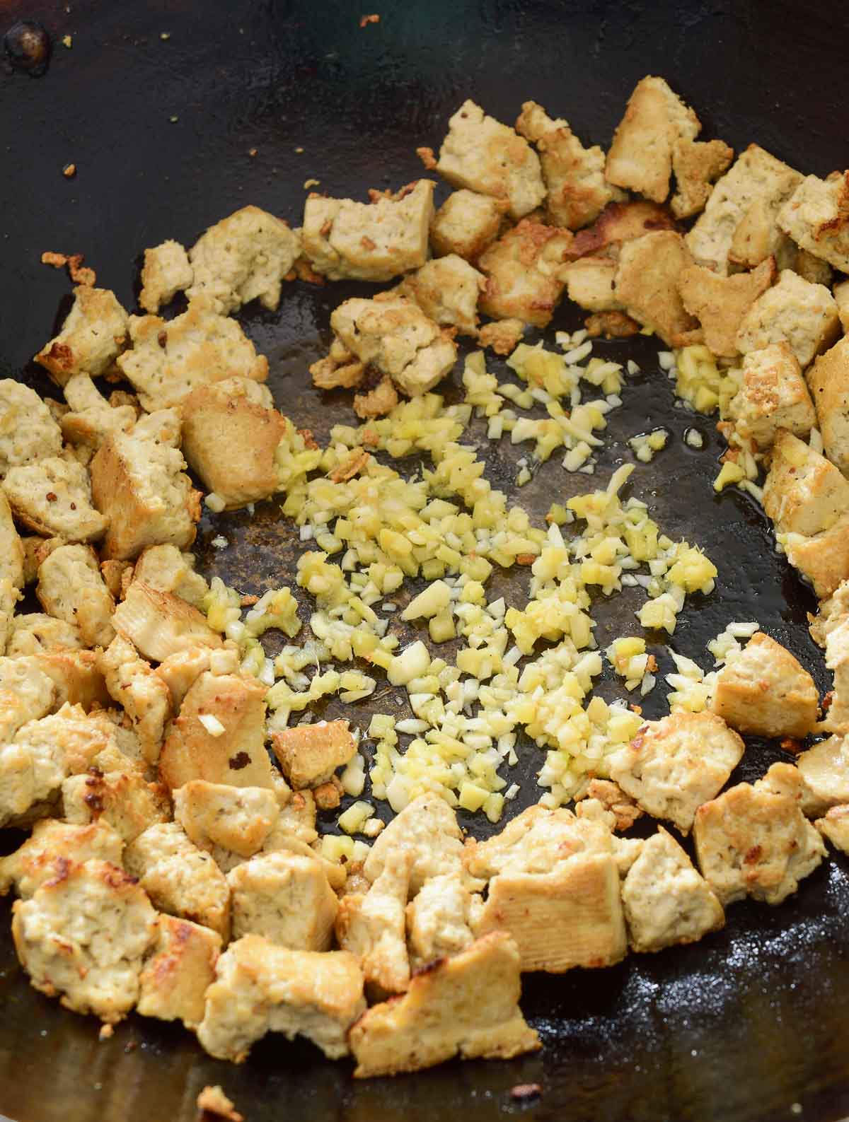The wok of fried tofu pushed to the side with minced ginger and garlic in the middle of the wok.