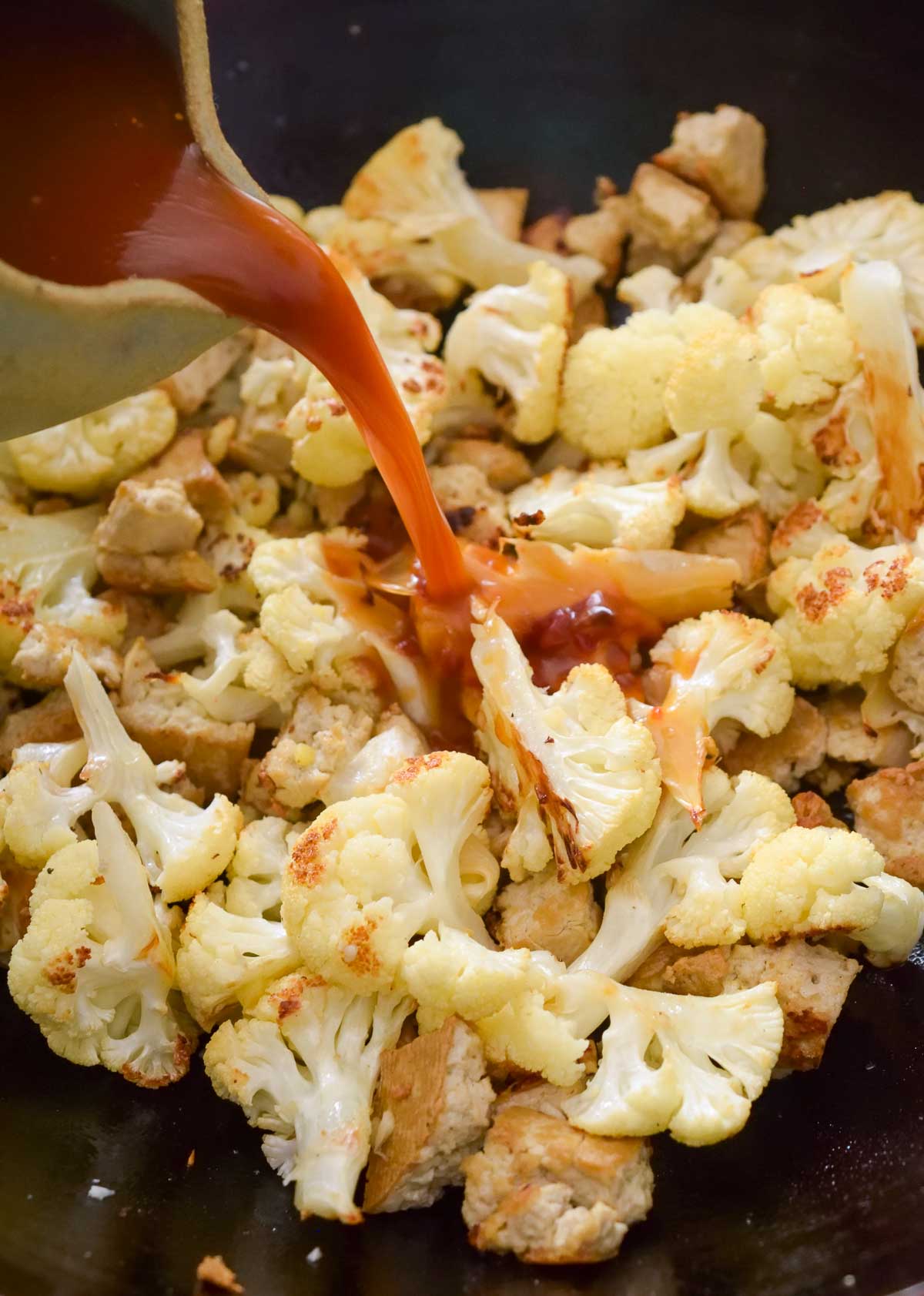 Pouring the vegan stir fry sauce into a wok with tofu and cauliflower.