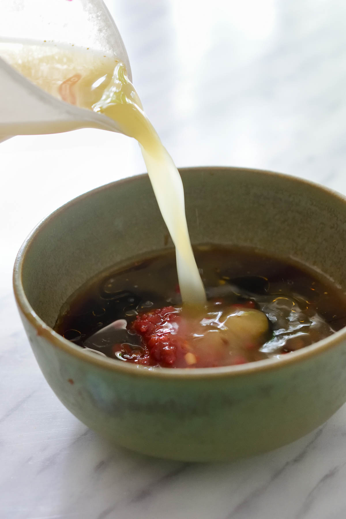 A green ceramic bowl with vegetable stock being poured into the vegan stir fry sauce.