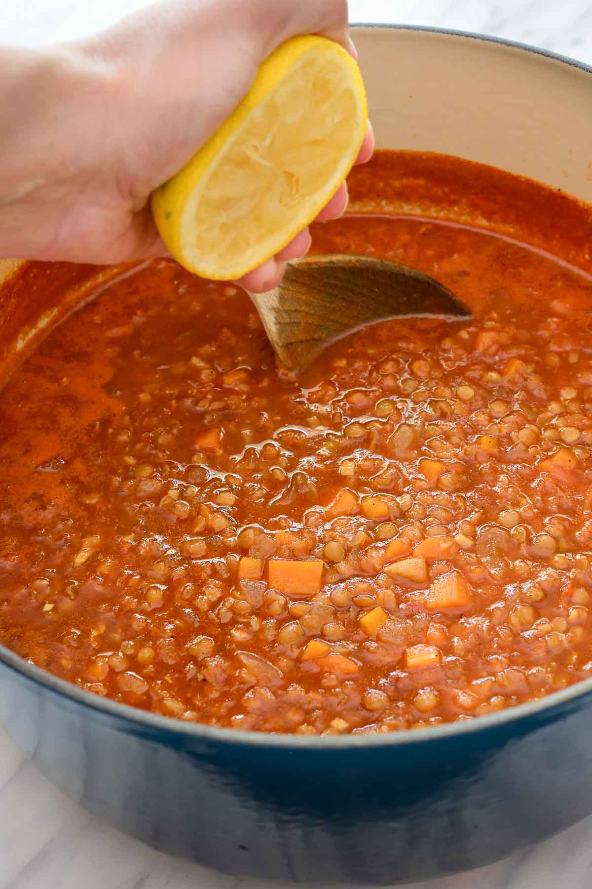 A hand is squeezing half a a lemon into the pot of Moroccan lentil soup.