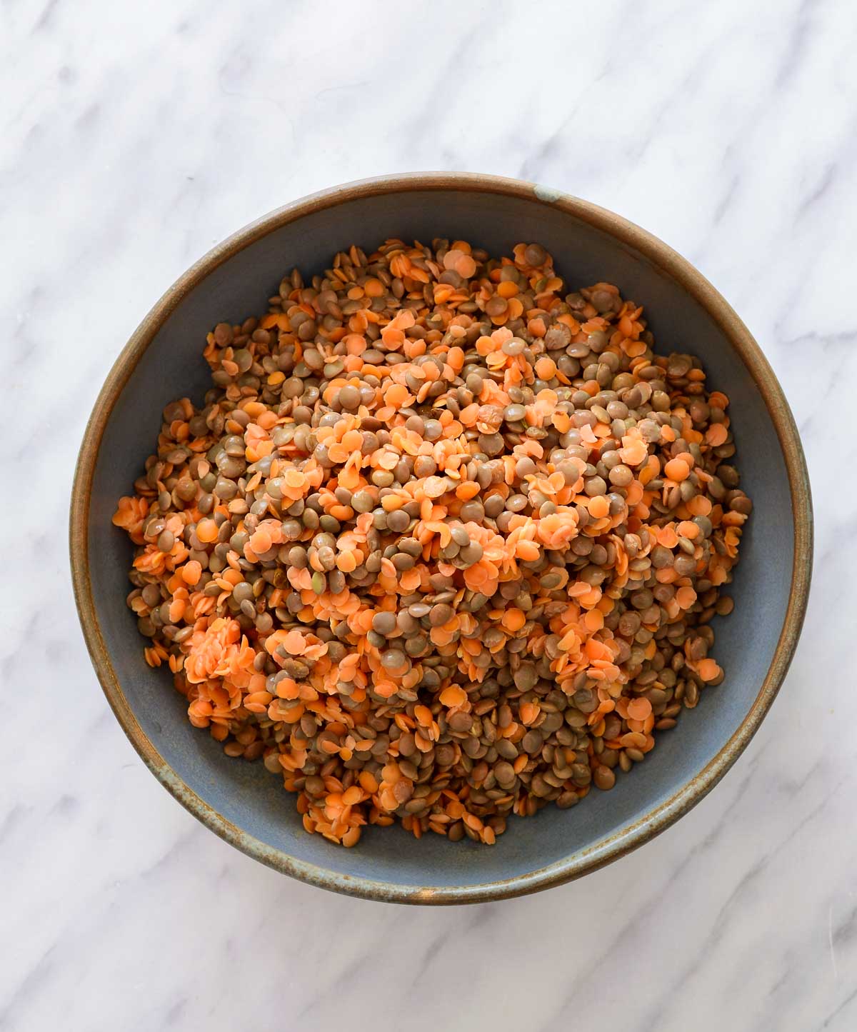 A blue bowl filled with a mix of red and brown dried lentils.