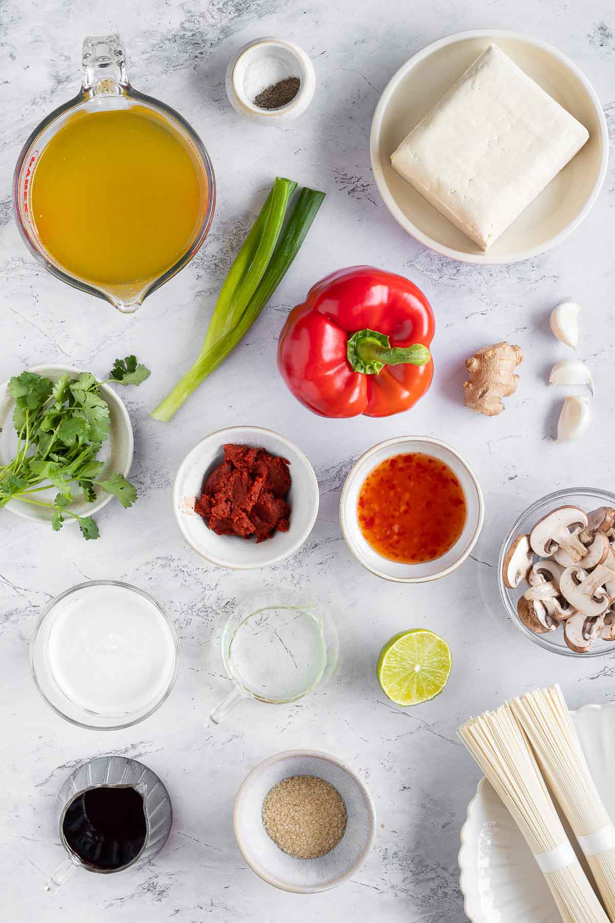 All the ingredients for this Thai ramen are displayed in small bowls on a white marble surface.