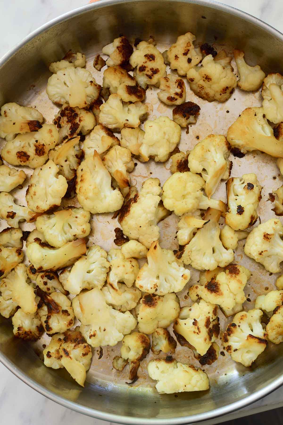 A silver pan filled with charred stir fried cauliflower florets.