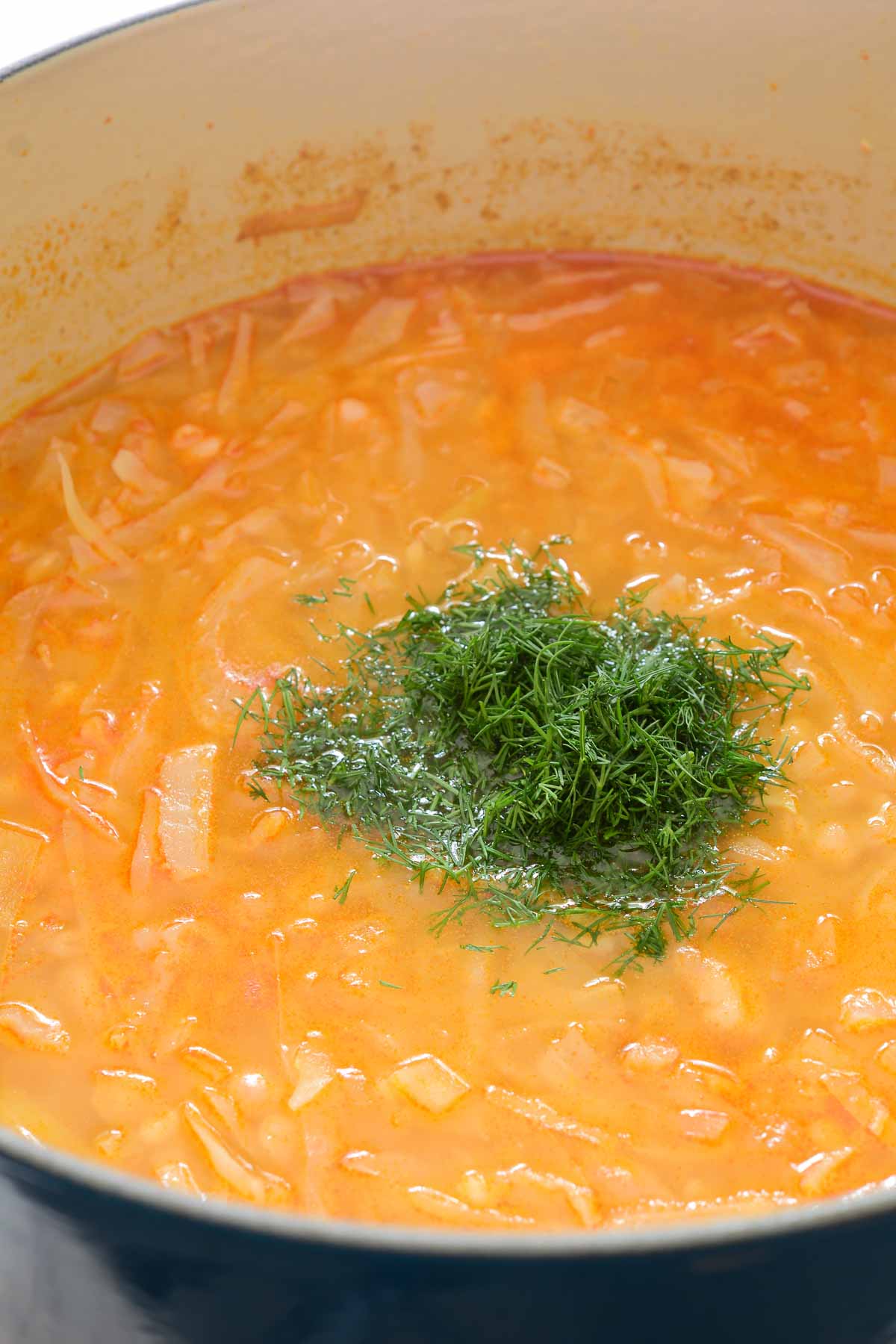A pile of fresh dill in the middle of a pot of cabbage and barley soup