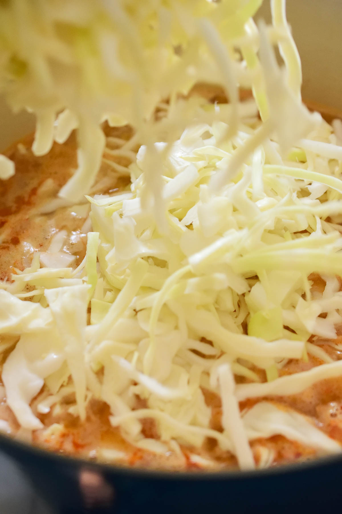 Pouring shredded cabbage into the pot of cabbage and barley soup.