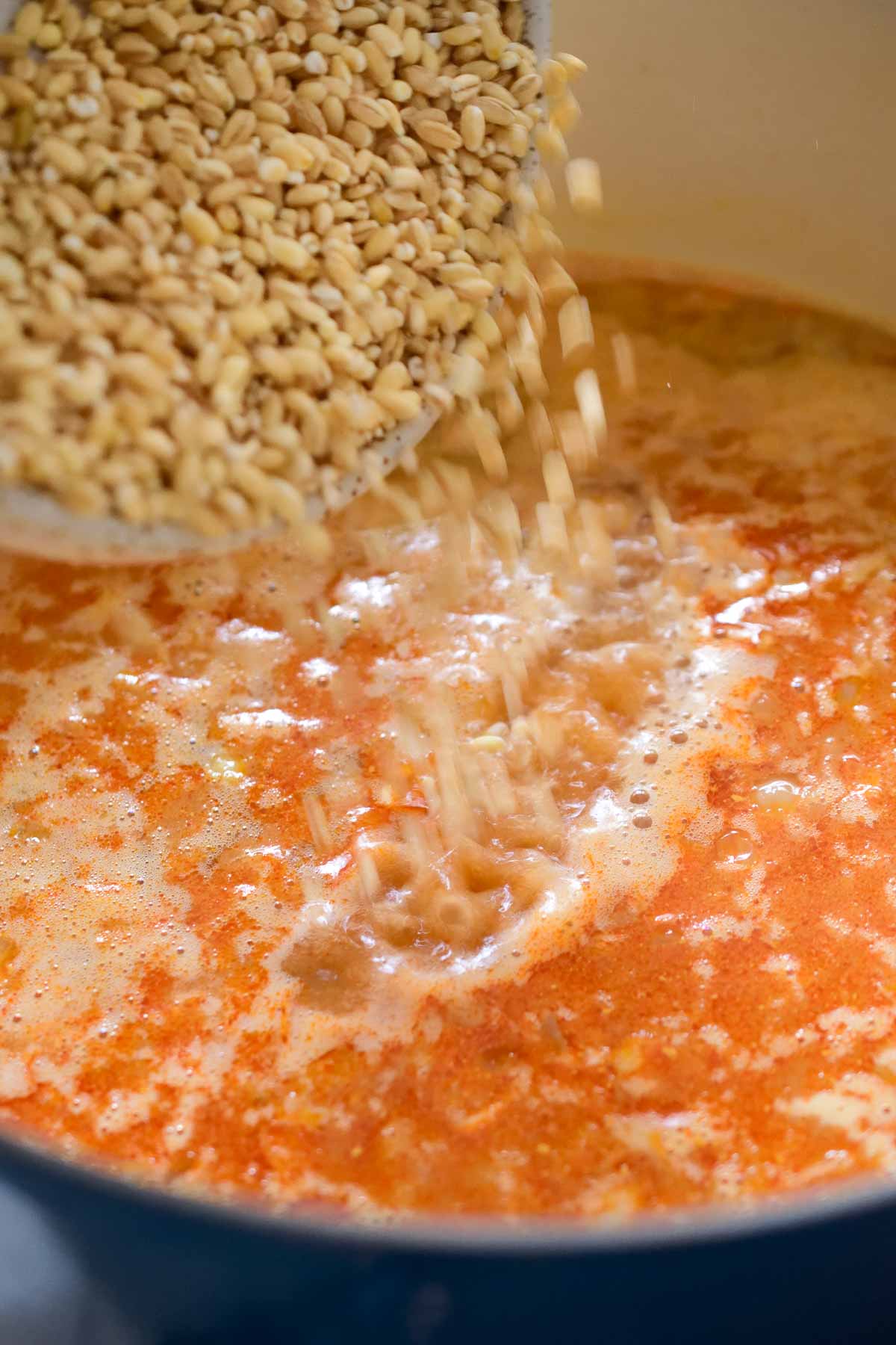 Pouring a bowl of barley into the cabbage and barley soup pot.