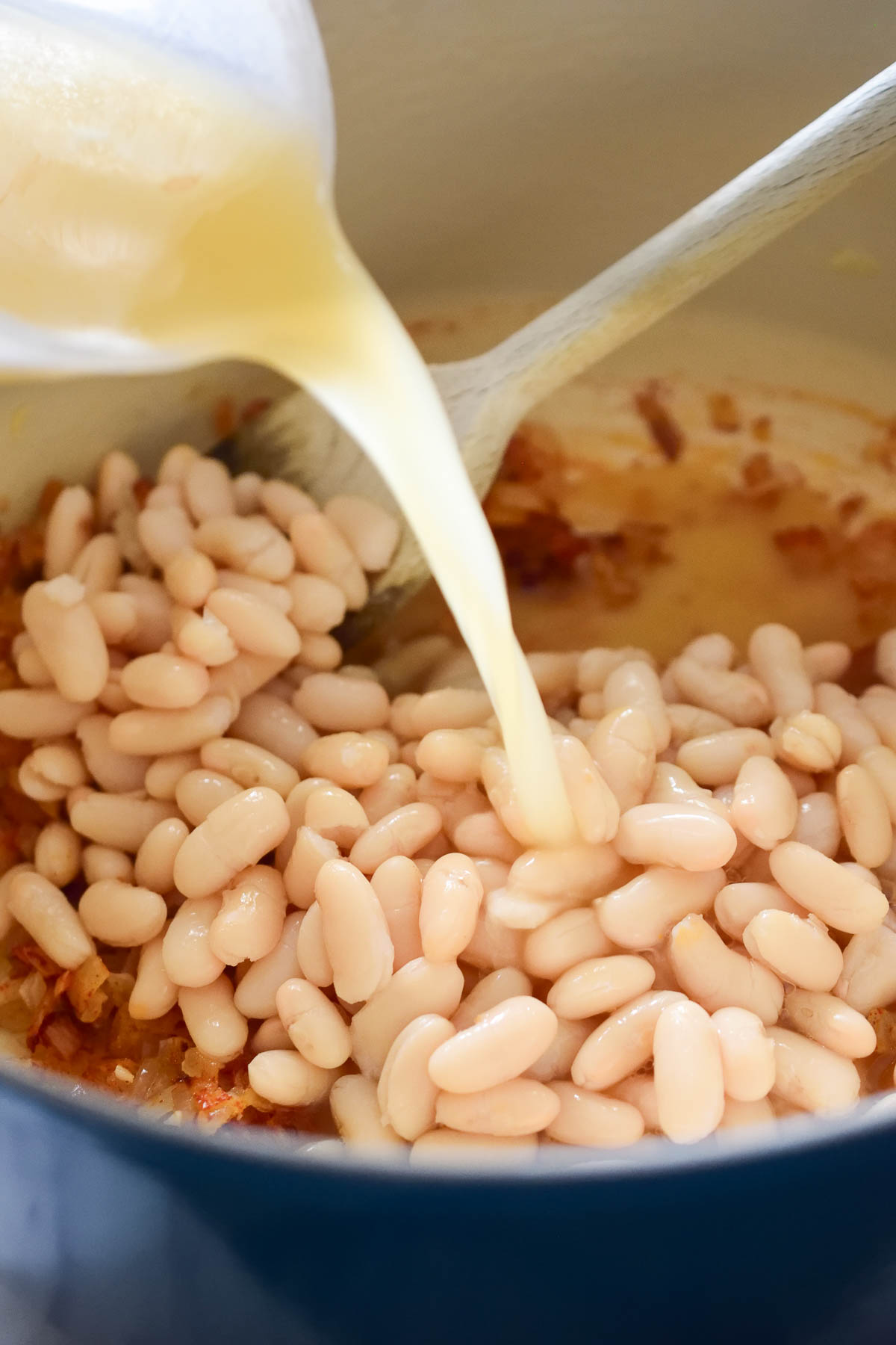 Pouring vegetable stock into a pot filled with white beans.