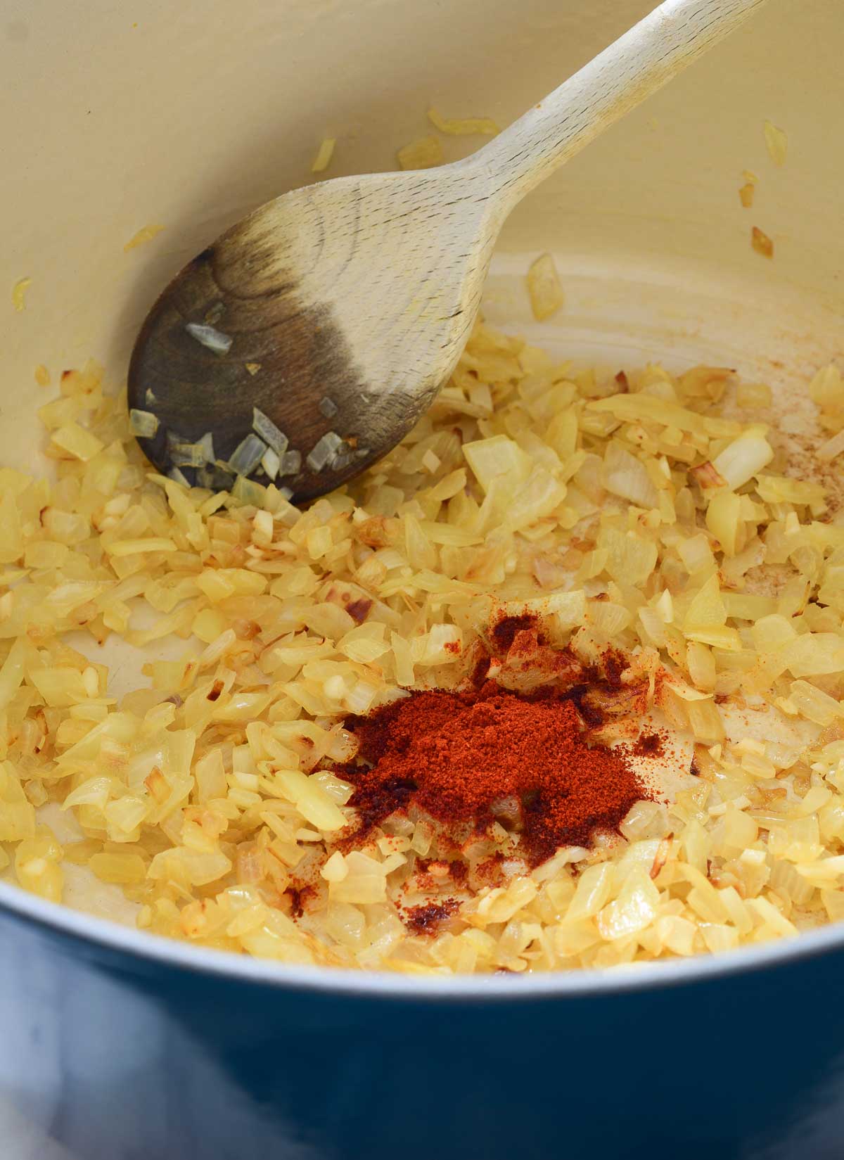 Inside a pot with fried onions and a pile of smoked paprika in the middle. A wooden spoon at the back.