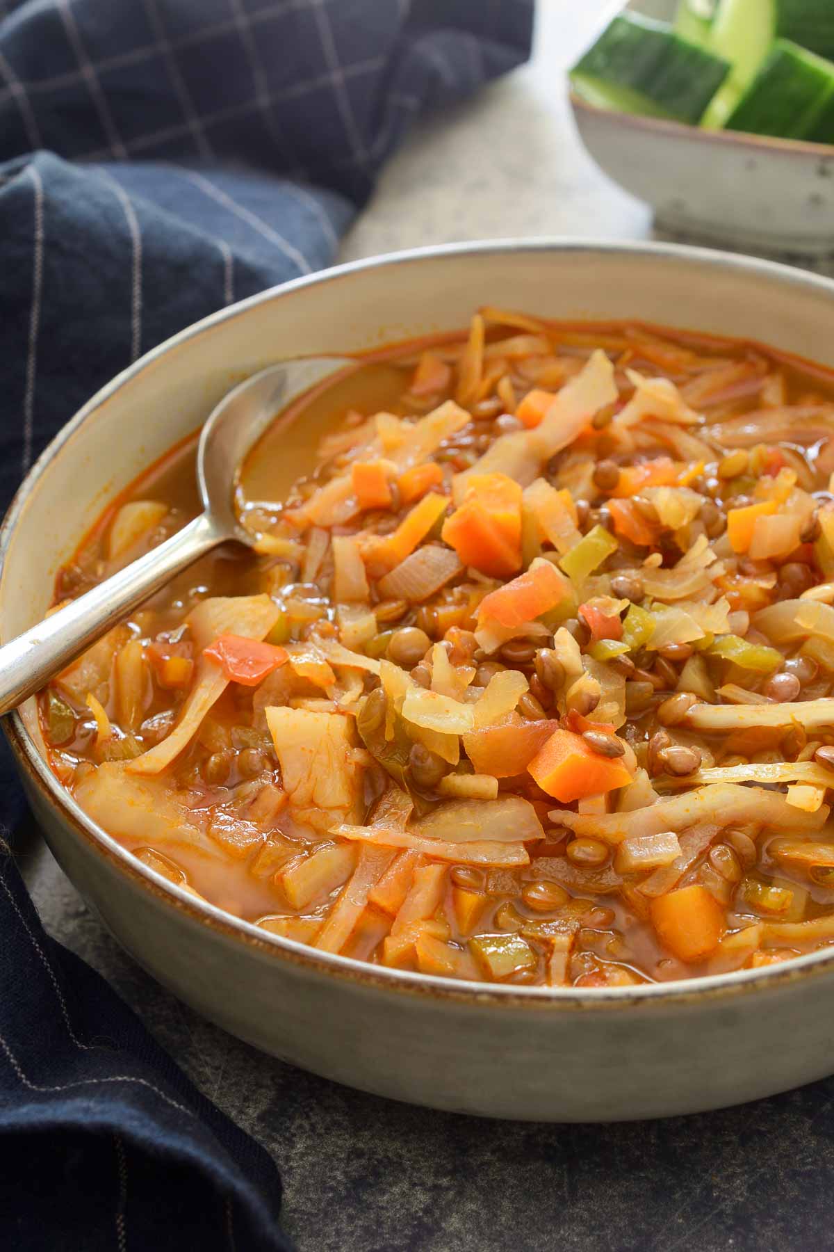 A grey ceramic bowl with a spoon resting inside filled with cabbage lentil soup.