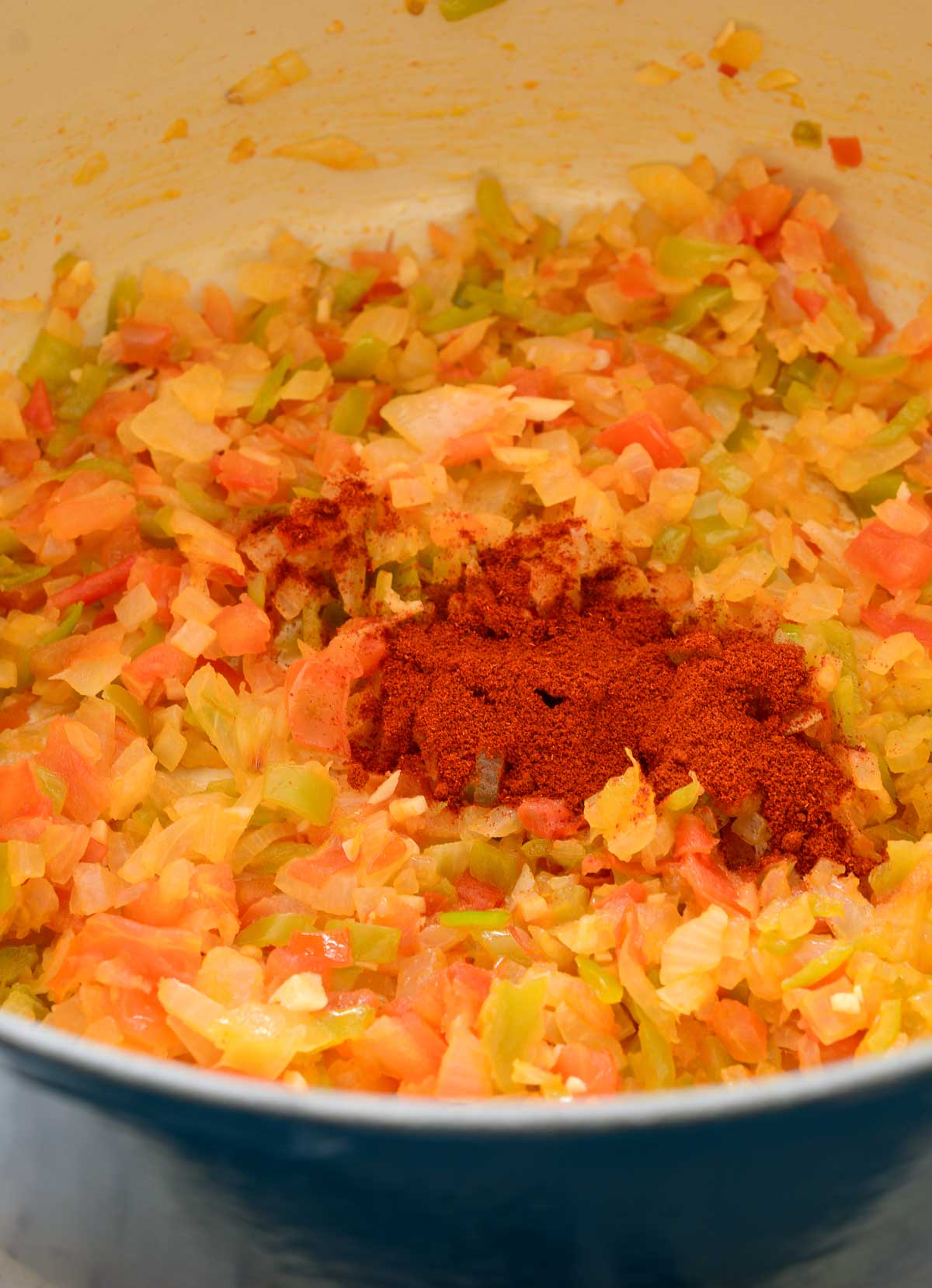 The fried onion, tomato and green pepper with a pile of smoked paprika in the middle in a blue pot.