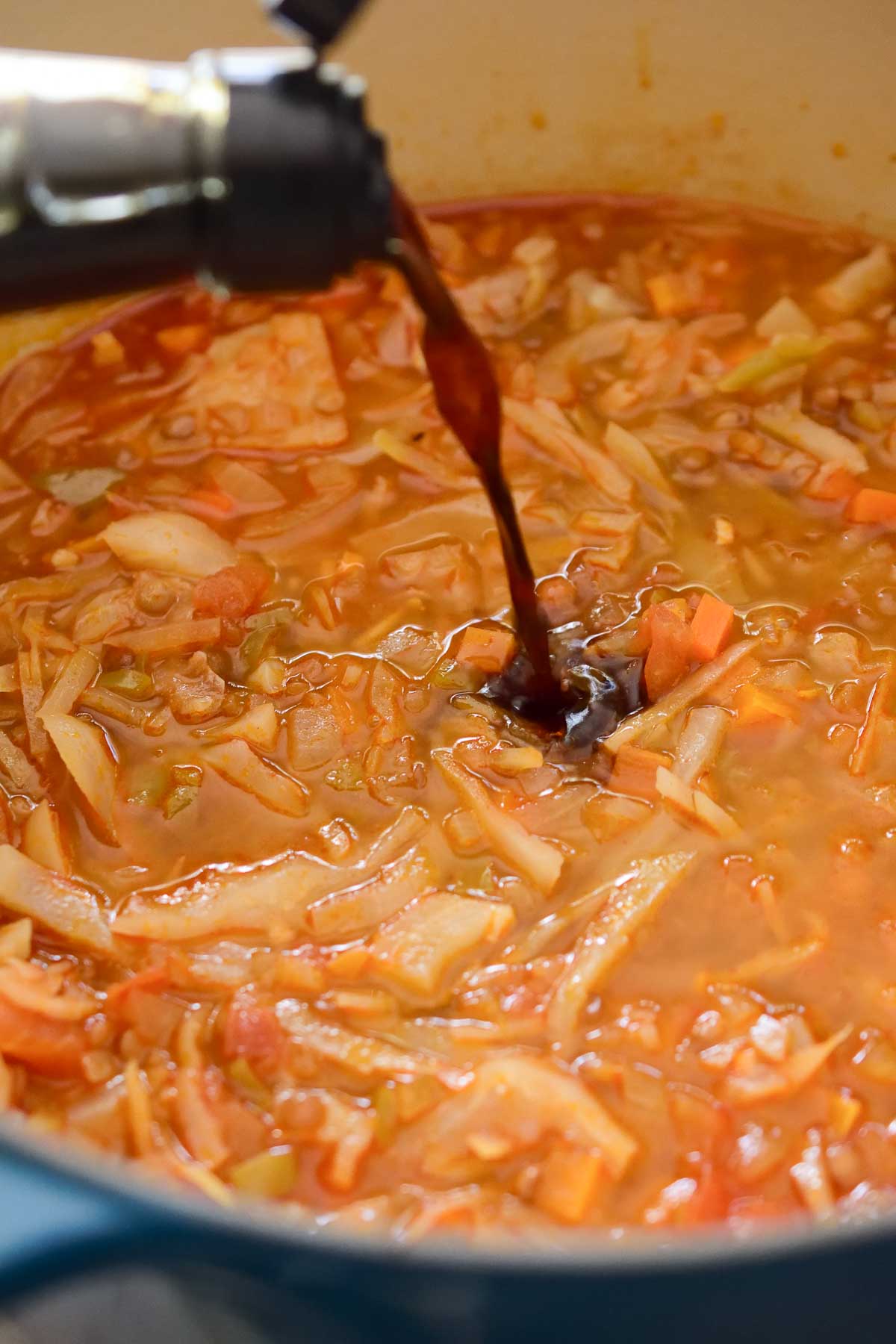 Pouring soy sauce into a pot filled with cabbage lentil soup.
