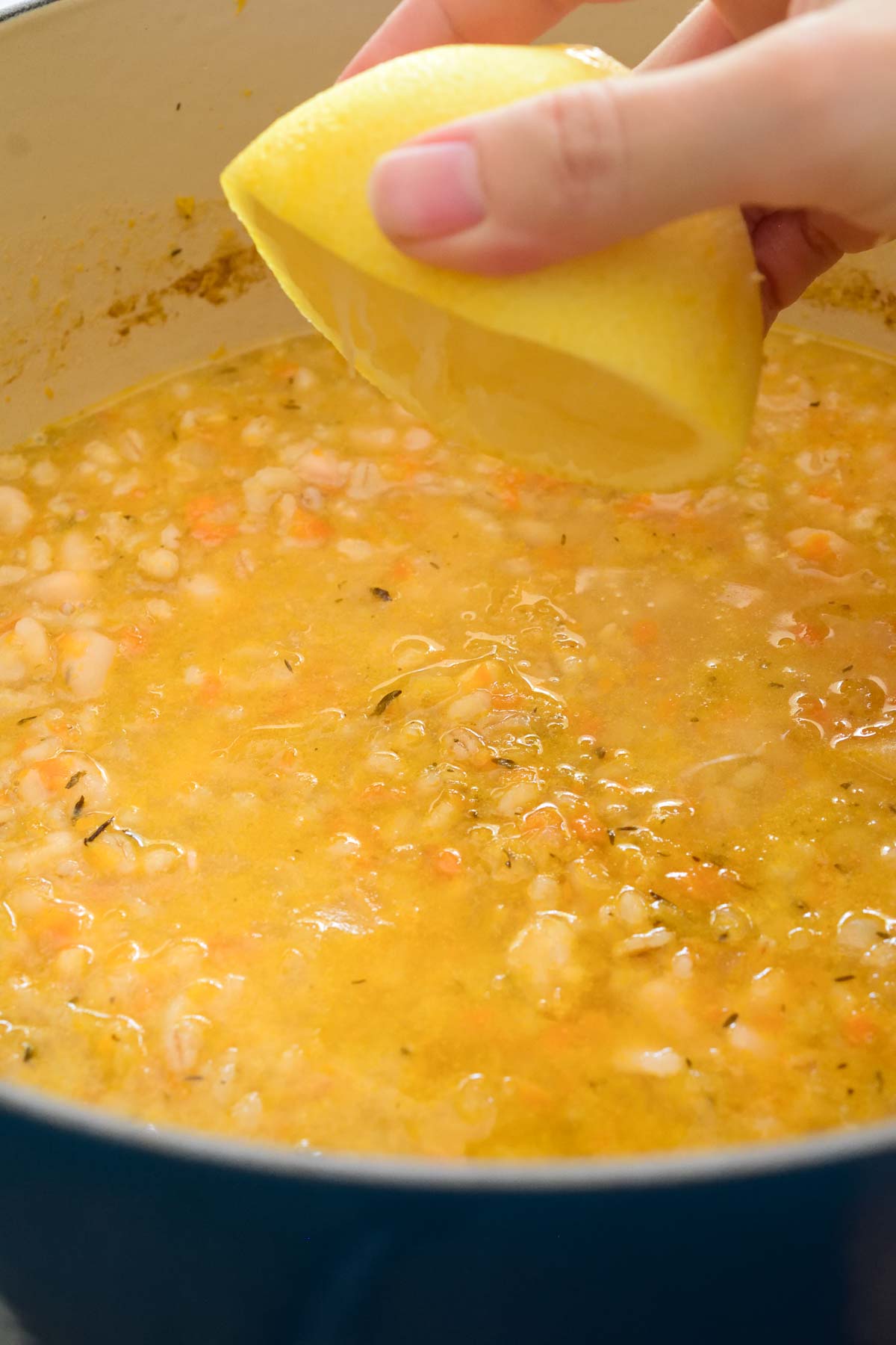 A hand squeezing half a lemon over the pot of lemon barley soup.