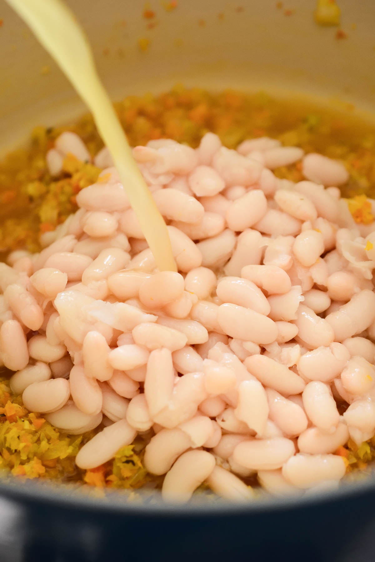 Inside the blue Dutch oven are the mirepoix, white beans and vegetable stock being poured in.