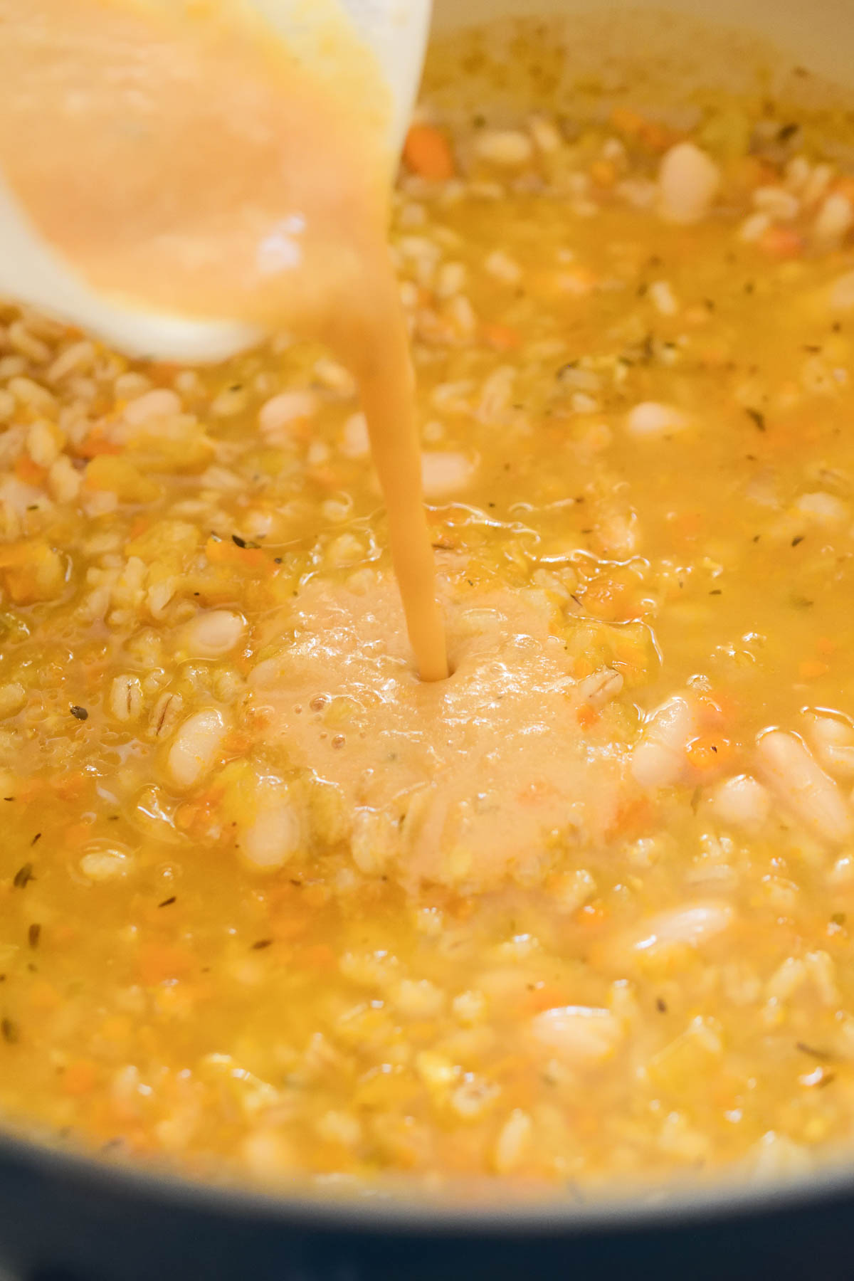 Pouring almond butter into the soup of lemon barley soup.