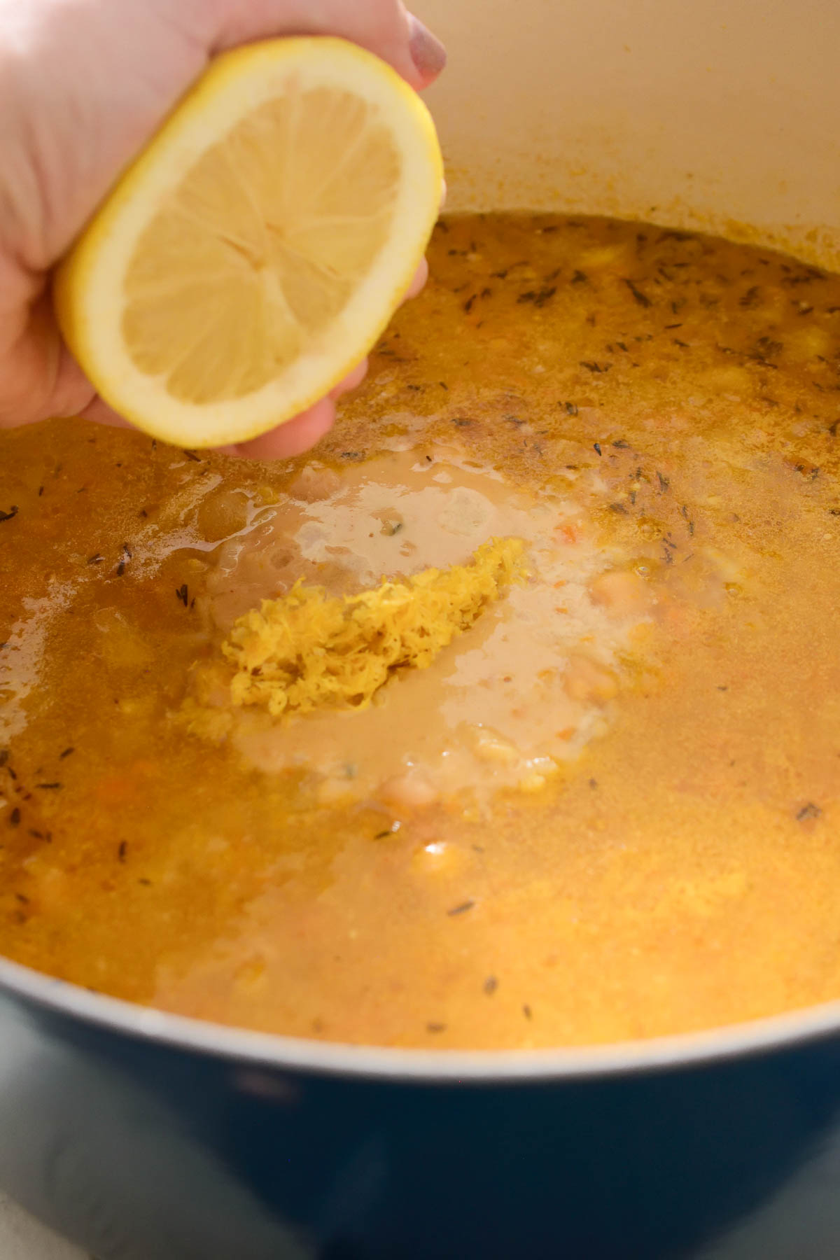 A hand squeezing half a lemon over the pot of lemon rice soup.
