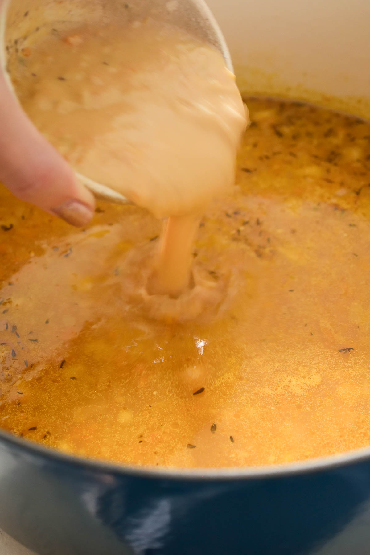 A hand holding a glass bowl and pouring almond butter into the pot of lemon rice soup.