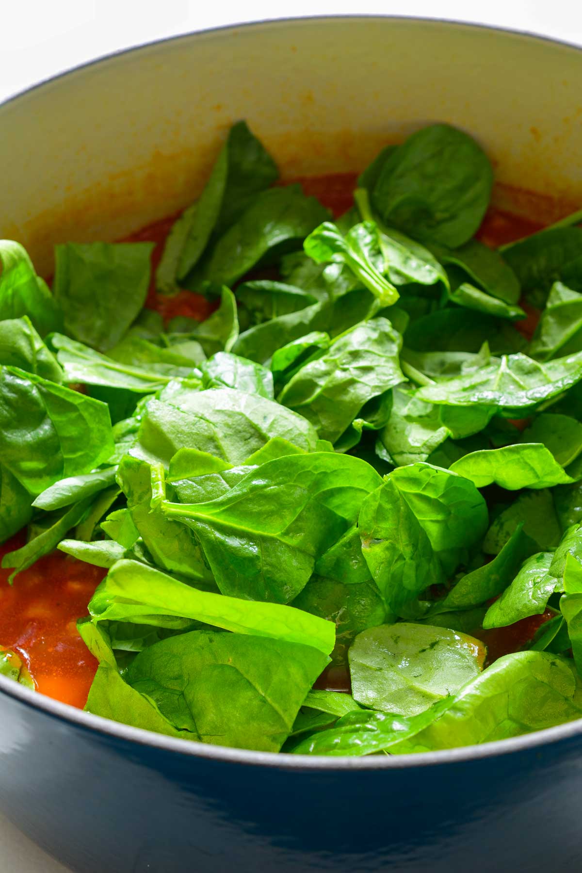 Leaves of fresh spinach in a blue pot of bean and barley soup.